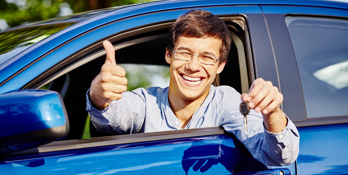 A young man giving a thumbs up after getting approved for a car loan.